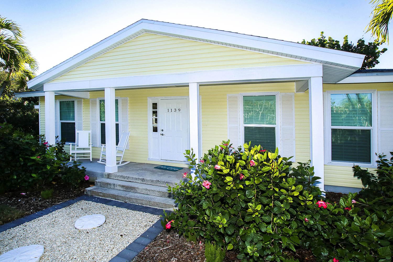 A yellow house with white trim and flowers in front of it.